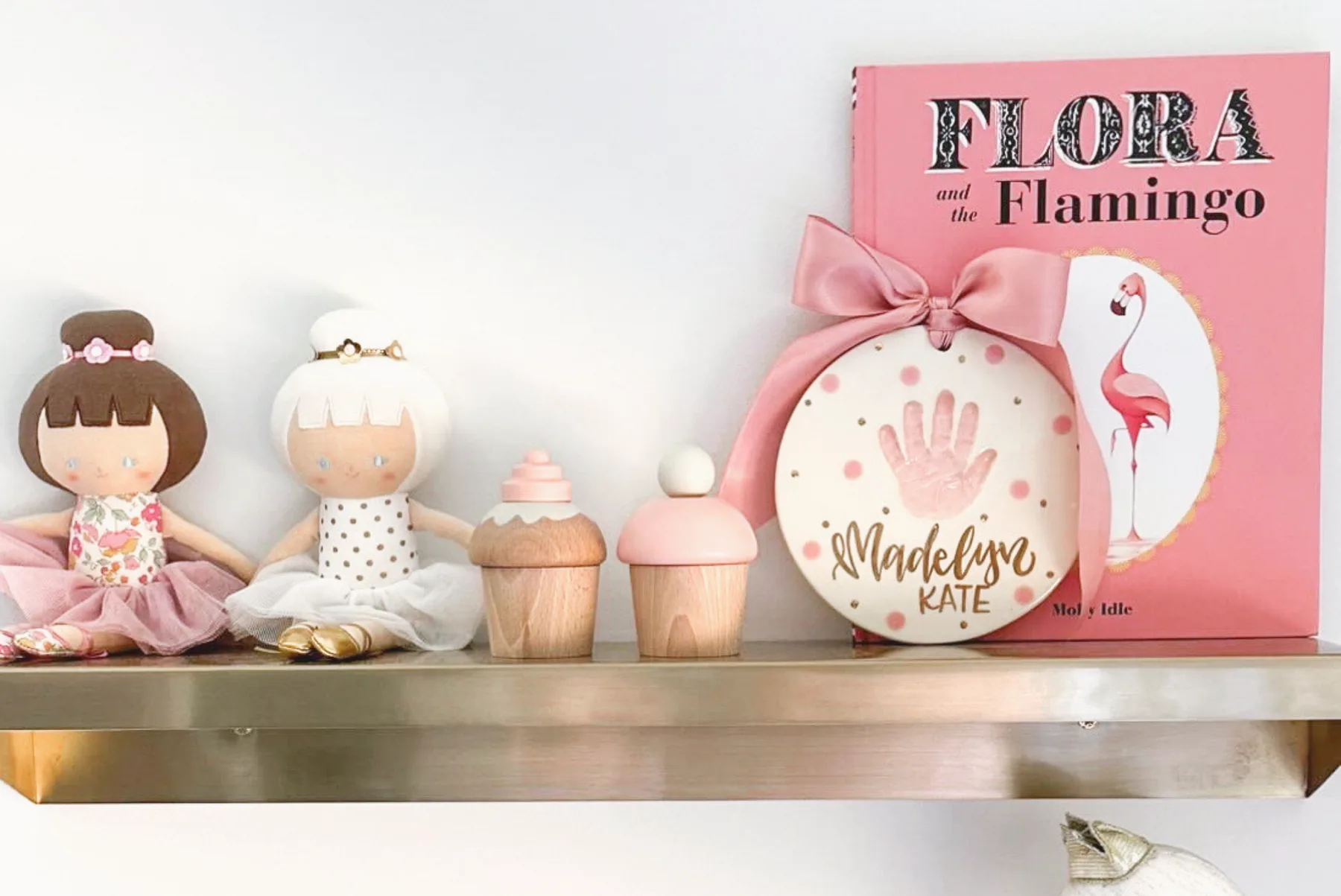 A hand-painted clay keepsake with a baby handprint, hung with a pink ribbon on a shelf